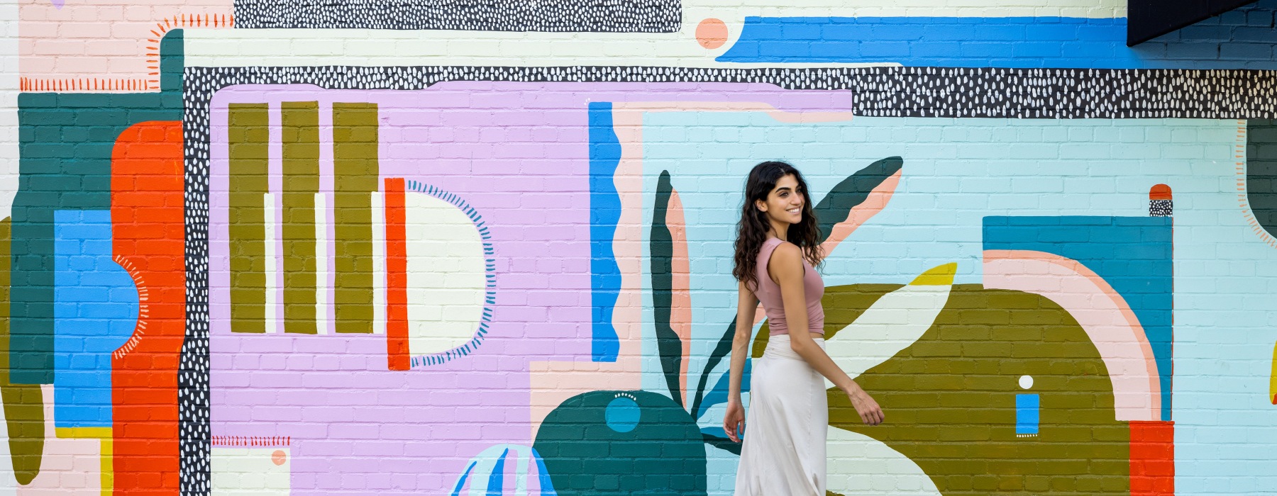 woman walking in front of mural