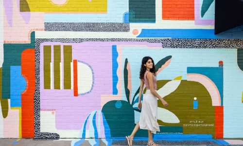 woman walking in front of mural